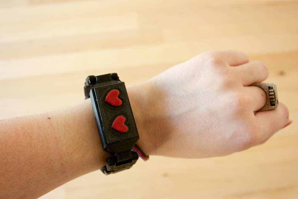 chunky black plastic bracelet worn on posed wrist, with 2 red 8-bit style hearts embossed on top of bracelet